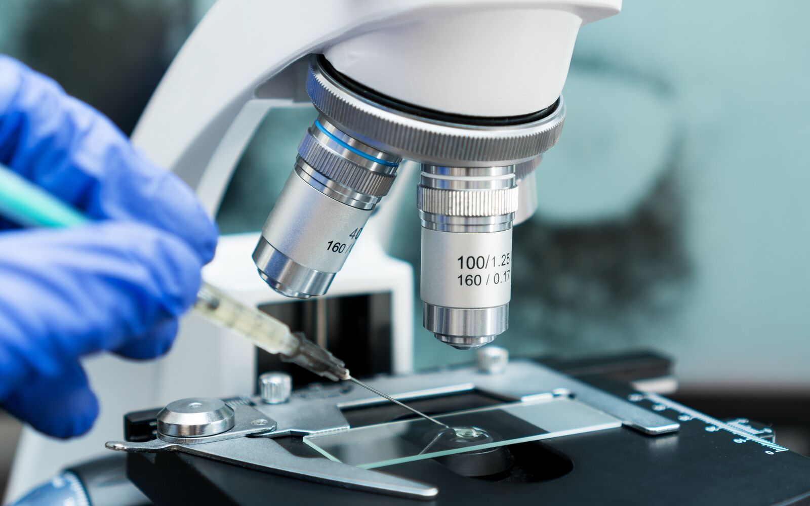 Virologist's hand in glove testing coronavirus vaccine under microscope.; Shutterstock ID 1699547959; purchase_order: Main Visual; job: ; client: ; other: